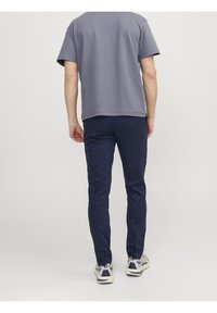 Grå kortärmad skjorta i kombination med navy slim-fit byxor och grå sneakers. Skjortan har en rundad fåll och mjuk textur.