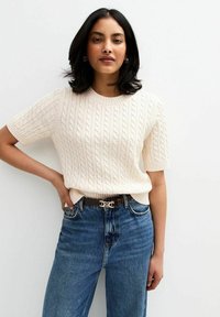 Kremowy sweter robiony na drutach z krótkimi rękawami, z teksturowanym wzorem w warkocz. Połączony z jeansami w kolorze niebieskim o wysokim stanie i brązowym paskiem.