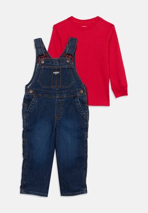 Une chemise rouge à manches longues associée à une salopette en jean bleu foncé, présentées à plat sur un fond clair.