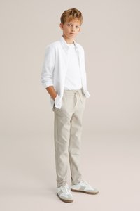 Balta pogājamā krekla virsbalta T-kreklu, apvienots ar bēšiem biksēm ar aukliņu un baltiem sporta apaviem ar pelēkām akcentiem. Vienkāršs un tīrs dizains.