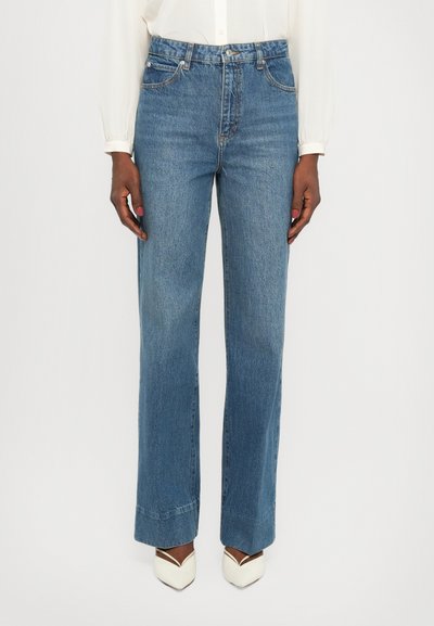Hellblaue Jeans mit hoher Taille, weitem Bein, Gürtelschlaufen und Fünf-Taschen-Design; passende weiße spitz zulaufende Absätze.