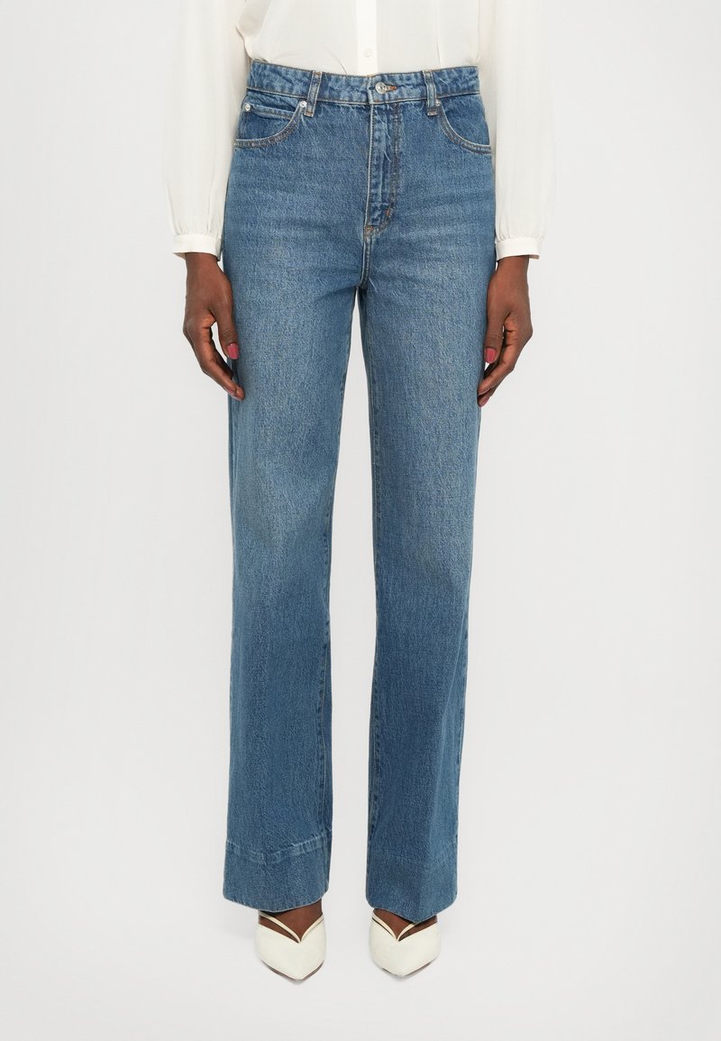 Light blue denim jeans with a high waist, wide-leg style, belt loops, and five-pocket design; matching white pointed-toe heels.