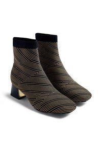 Botines de punto negros y dorados con un patrón geométrico, puntera afilada y tacón cuadrado con un acento dorado. La parte superior tiene un puño acanalado.