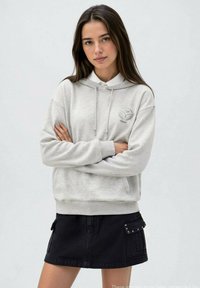 Felpa grigia con cappuccio e coulisse, dotata di tasca frontale; abbinata a una gonna di jeans nera con tasche laterali.