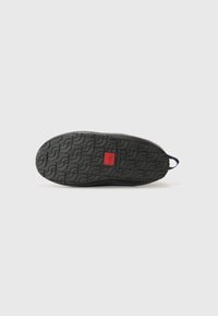 Semelle de chaussure en caoutchouc noir avec motif de crantage, comportant une étiquette logo rouge au centre. Bords lisses et boucle de renforcement au talon pour un enfilage facile.