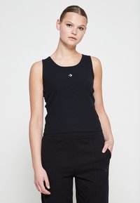 Débardeur noir côtelé avec un col rond, présentant un petit logo blanc sur la poitrine. Associé à un pantalon noir.