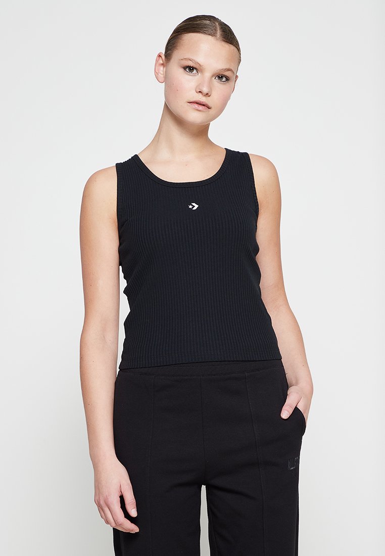 Débardeur noir côtelé avec un col rond, présentant un petit logo blanc sur la poitrine. Associé à un pantalon noir.