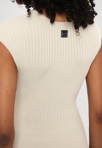 Ribbed, beige dress with a fitted silhouette, featuring cap sleeves and a small black logo tag near the neckline. Smooth texture.