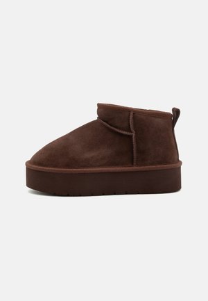 Brown suede ankle boot with a rounded toe, soft texture, and a thick platform sole. Features a subtle seam detail and a back pull tab.