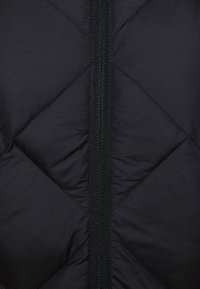 Sort quiltet stof med en central sort lynlås, der viser et diamantformet syningsmønster på materialet.