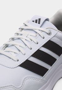 Weißer Turnschuh mit schwarzen Streifen, weißen Schnürsenkeln und einem dreieckigen Logo auf der Zunge, Nahaufnahme der Oberseite.