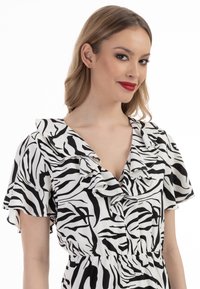 Ung kvinde med bølget blond hår, rød læbestift og en sort-hvid zebra print kjole med flæset halsudskæring og korte ærmer.