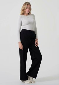 Lys grå langermet crop topp med liten tekst på brystet, sammen med vide svarte bukser med snor i livet. Nøytrale sneakers.