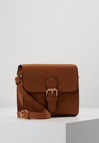 Brązowa torba na ramię z ekologicznego zamszu z klapką, złotym zatrzaskiem i regulowanym paskiem. Prostokątny kształt o gładkiej fakturze.