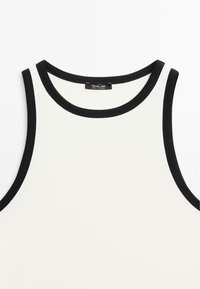 White tank top with black trim and wide shoulder straps. Soft fabric with a round neckline and a tag sewn onto the inner collar.