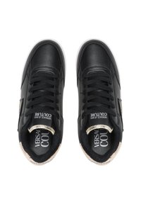 Baskets en cuir noir avec une finition texturée, semelles en caoutchouc blanc, accents dorés sur le talon et lacets plats noirs. Marque Versace visible.