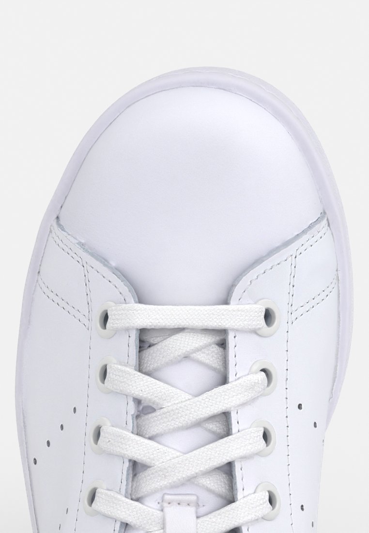 Baskets blanches avec une tige en cuir lisse, des lacets plats, un bout rond et de petites perforations sur les côtés pour la respirabilité.