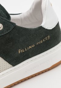 Green suede sneaker with white leather accents, perforated details, gold "Filling Pieces" logo, and textured rubber sole.