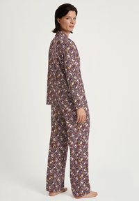 Lange, paarse pyjama set met bloem- en dierenpatronen. Glad materiaal met lange mouwen en broeken, met een chemise ontwerp met knopen.