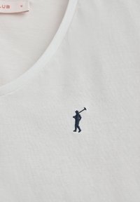 Maglietta bianca di cotone con una figura ricamata di colore blu navy che porta uno strumento, design a scollo a V e tessuto morbido.