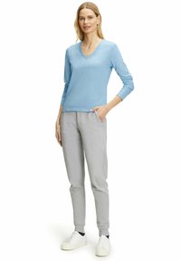 Helles blaues Langarm-V-Ausschnitt-Oberteil kombiniert mit grauen Sweatpants, die seitliche Taschen und elastische Bündchen haben. Weiße Sneaker vervollständigen das Outfit.