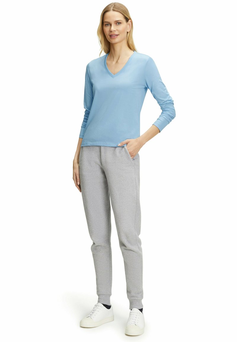 Helles blaues Langarm-V-Ausschnitt-Oberteil kombiniert mit grauen Sweatpants, die seitliche Taschen und elastische Bündchen haben. Weiße Sneaker vervollständigen das Outfit.