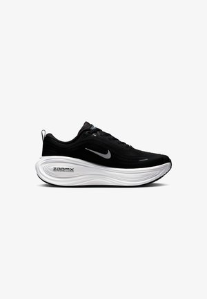 Chaussure de sport noire avec une tige texturée, semelle blanche rembourrée et semelle extérieure noire contrastante. Comprend un logo réfléchissant et un système de laçage.