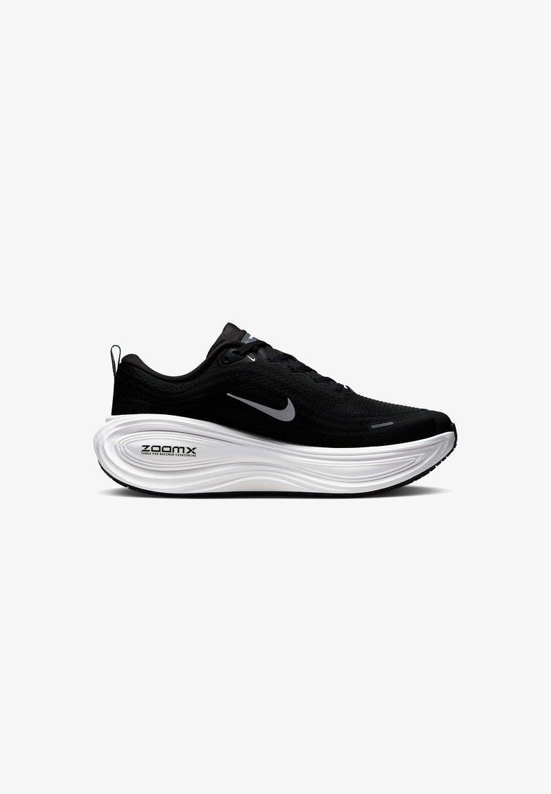 Chaussure de sport noire avec une tige texturée, semelle blanche rembourrée et semelle extérieure noire contrastante. Comprend un logo réfléchissant et un système de laçage.