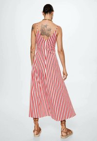 Combinaison rayée rouge et blanche avec des bretelles spaghetti, un dos en V et des jambes larges. Caractéristiques d'un corsage ajusté et d'une coupe décontractée, fabriquée en tissu léger.