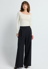 Off-white lange mouw top met een bootneck, gecombineerd met hoge taille zwarte wijde broek. Zwarte schoenen met gouden accenten.