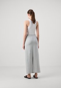 Lysegrå vide joggebukser med en komfortabel elastisk midje og en myk, glatt tekstur; kombinert med svarte sandaler.