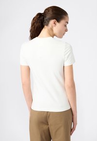 T-shirt bianca a maniche corte con scollatura rotonda, texture liscia e forma aderente, vista dal retro su uno sfondo chiaro.