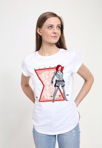 Hvid t-shirt med et grafisk print af en karakter i en grå dragt med røde accenter, sat mod et rødt timeglasdesign.