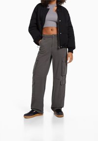 Černá péřová bunda, šedý strakatý crop top, šedé cargo kalhoty s kapsami a černé tenisky s gumovými podrážkami. Jednoduchý, utilitární styl.