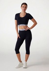 Top sport crop bleumarin cu decolteu rotund și mâneci scurte, asortat cu colanți cu talie înaltă care au logo contrastant pe banda de talie.