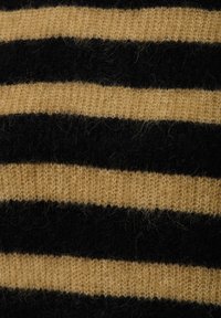Close-up van gebreide stof met afwisselende fuzzy zwarte en tan horizontale strepen.