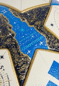 Gros plan d'une section en forme d'étoile bleue et dorée sur un ballon de match de compétition replica, avec des motifs étoilés et une surface texturée.
