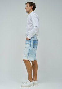 Shorts de mezclilla azul claro con un acabado desgastado, bolsillos delanteros y traseros, y un ligero detalle de desgaste. Combinados con zapatillas blancas y una camiseta blanca.