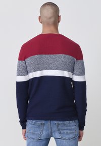 Maglione da uomo con una texture a coste, design a blocchi di colore in rosso, grigio, bianco e blu navy. Collo rotondo e maniche lunghe.