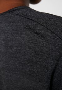 Black fabric shirt with a textured surface and a discreet "Houdini" logo near the shoulder seam, featuring a simple design and casual fit.