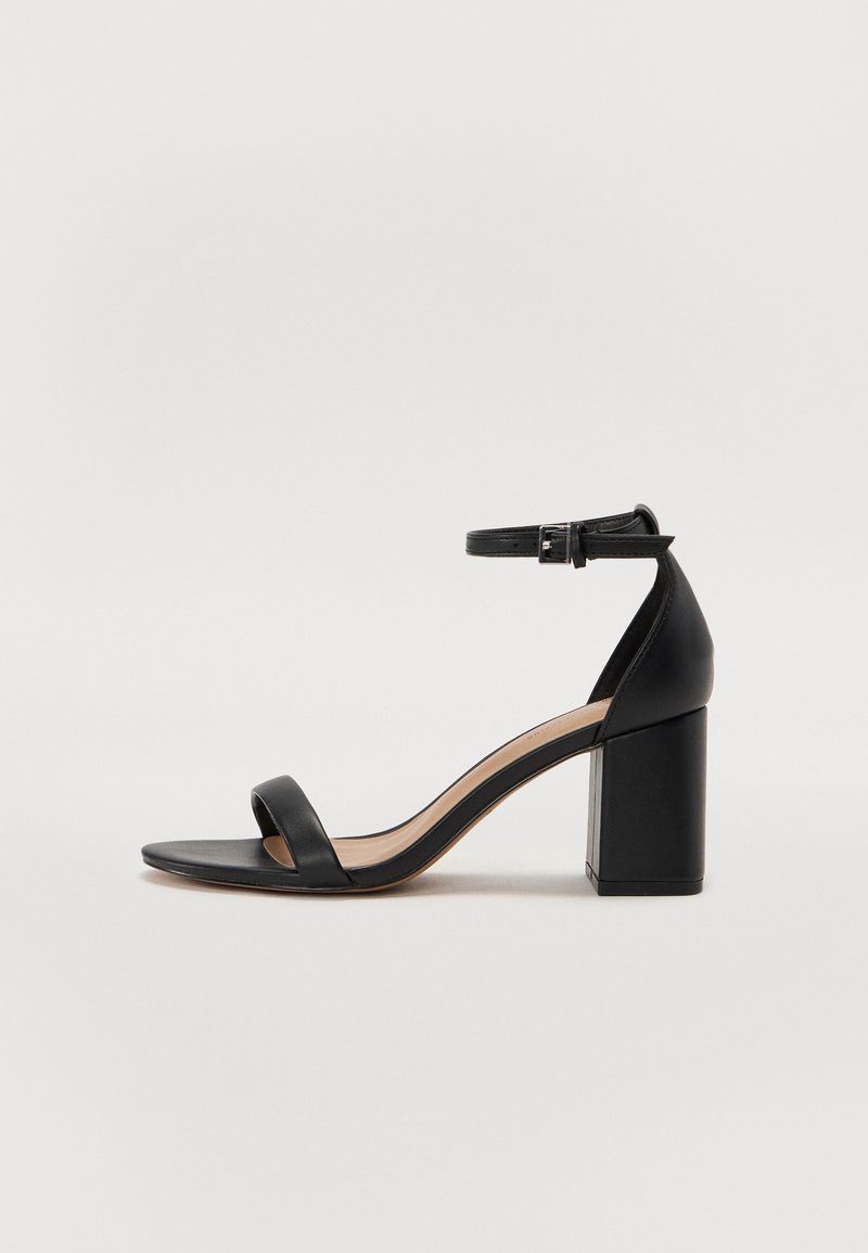 Sandale noire à talon haut avec bride cheville et boucle, talon bloc, et une seule lanière sur les orteils, vue de profil sur fond blanc.