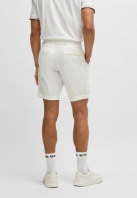 White cotton shorts with a straight cut and rolled hem, featuring two back pockets. Worn with white sneakers and patterned socks.