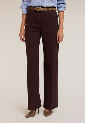 Vrouw draagt donkerbruine wijde broek met hoge taille, lichtbruine riem, gestreept blauw overhemd en beige hoge hakken.