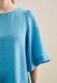 Top in lino blu con ampie maniche corte fluide e scollatura rotonda. Il tessuto ha una texture morbida con una trama sottile.