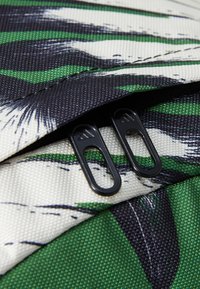 Textured fabric in green, black, and white with a leaf pattern. Features black zipper pulls with an Adidas logo.