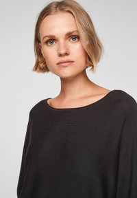 Zwarte gebreide trui met een losse, brede halslijn en lange mouwen, met een gladde textuur en een ontspannen silhouet.