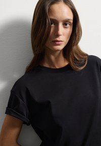 Maglietta nera a maniche corte con risvolti, realizzata in tessuto morbido. Design a girocollo con vestibilità rilassata, esposta su uno sfondo neutro.