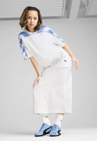 Valge liibuvast suurema lõikega t-särk, mille õlgadel sinine muster, kombineeritud pika valge seelikuga. Hele sinised tennised ja valged sokid mustade detailidega.