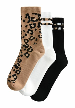 Three pairs of socks: one tan with black leopard spots, one solid white, and one solid black, all with ribbed texture and contrasting accents.