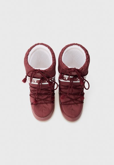 Botas acolchadas rojas que cuentan con un diseño cosido, parte superior elástica, flecos decorativos y una marca blanca en contraste en la parte superior. Forro interior suave.